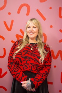 a woman in a red sweater standing in front of a pink wall